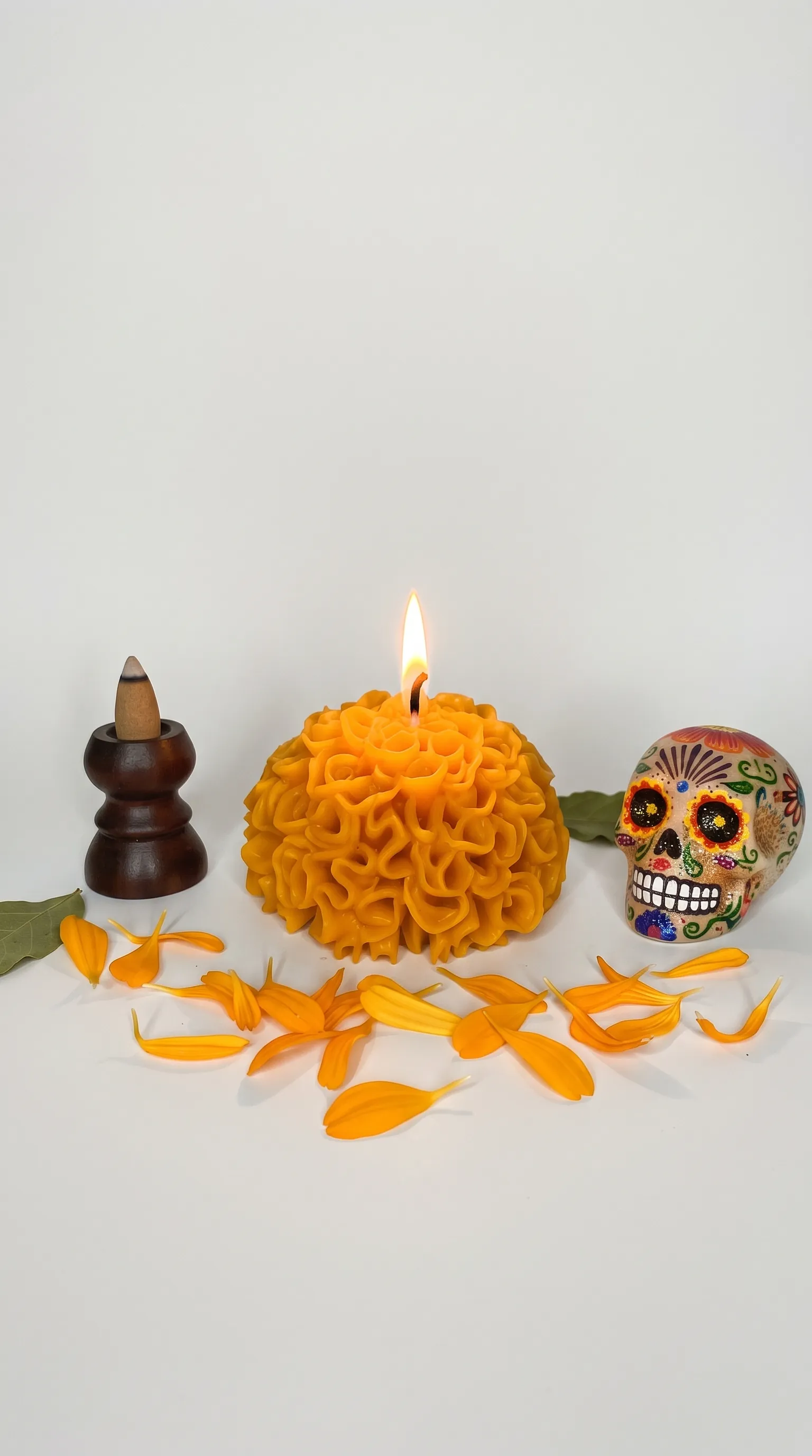 Vela de flor de cempasúchil encendida junto a un sahumerio, pétalos y una calaverita
